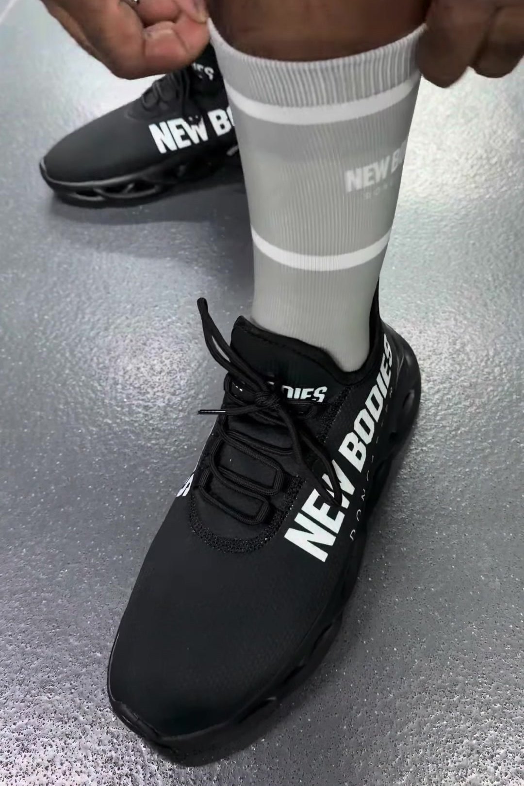 Black trainer with New Bodies on the side and a branded sock